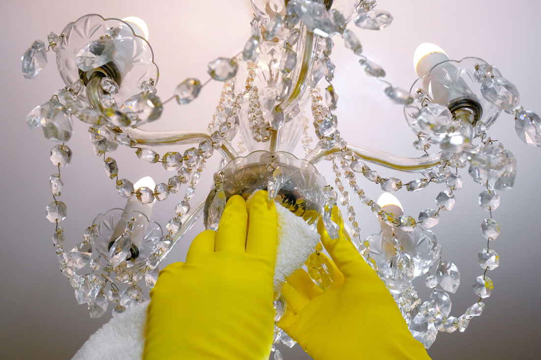 A person is cleaning a crystal luxury chandelier with white cloth