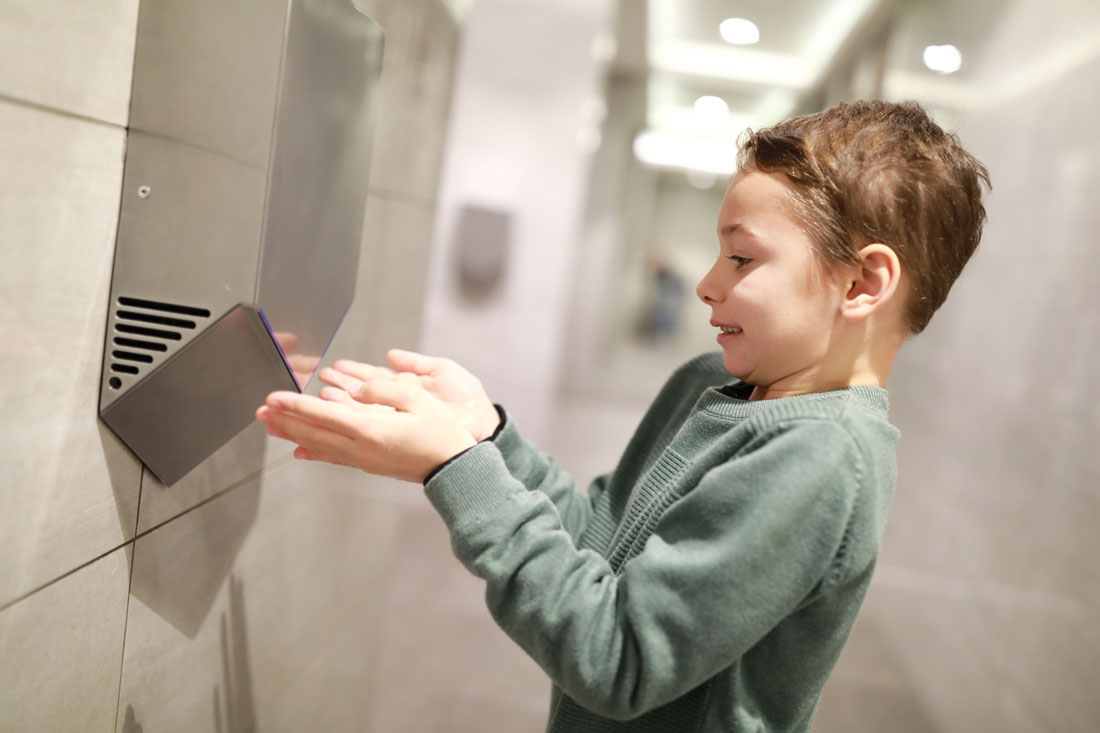 Boy dries his hands in the restroom using an electrical hand-dryer.

