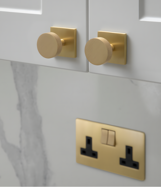 Pair of knurled Satin Brass circular cabinet knobs on square backplates, positioned above a matching Satin Brass double electrical socket.